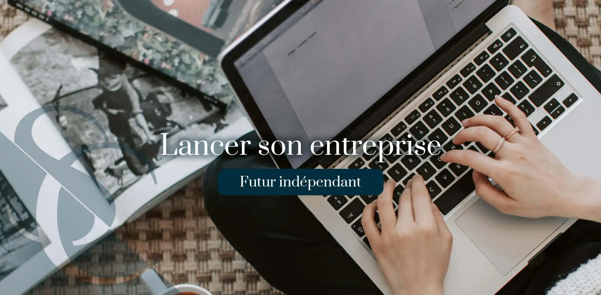 lancer-son-entreprise-belgique vu de haute, une femme tape sur som mac portable, elle est assie en tailleur et a une tasse de thé et des livres à cotés d'elle qui parle de lancer son entreprise